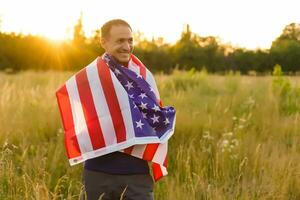il quarto di luglio. patriottico uomo con il nazionale americano bandiera nel il campo. giovane uomo con orgoglio agitando un americano bandiera. indipendenza giorno. foto