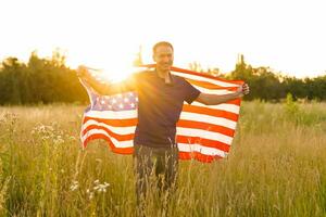 il quarto di luglio. patriottico uomo con il nazionale americano bandiera nel il campo. giovane uomo con orgoglio agitando un americano bandiera. indipendenza giorno. foto