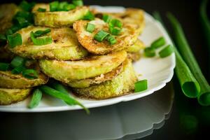 fritte zucchine nel cerchi con fresco erbe aromatiche nel un' piatto su un' nero foto