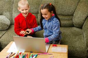 Due bellissimo carino contento sorridente figli, un' ragazzo e un' ragazza, uso il computer portatile per distanza apprendimento o intrattenimento. foto