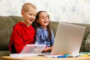 Due bellissimo carino contento sorridente figli, un' ragazzo e un' ragazza, uso il computer portatile per distanza apprendimento o intrattenimento. foto