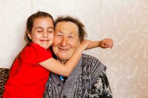 famiglia bonding concetto. bello poco ragazza felicemente abbracciare sua nonna nel leggero vivente camera foto