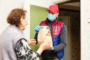 un anziano donna soggiorni a casa. cibo consegna nel un' medico maschera per il anziano. foto