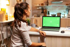 donna guardare a il computer portatile con verde modello durante notte tempo nel casa cucina. seduta a scrivania lavori su computer in ritardo a notte, attività commerciale, in linea, inteligente, vuoto, copyspace. foto