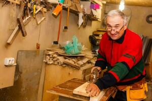 soddisfatto allegro gioioso sorridente maestro del legno è in piedi vicino del desktop nel il suo officina, stazione di lavoro foto