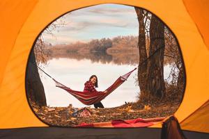 vista dalla tenda donna seduta sull'amaca con il lago sullo sfondo foto