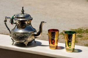 un' argento tè pentola e Due colorato tazze su un' tavolo foto