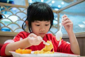 carino poco asiatico bambino ragazza mangiare cibo foto