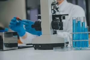 scienziato o medico nel laboratorio cappotto Lavorando nel biotecnologico laboratorio, microscopio attrezzatura per ricerca con miscelazione reagenti nel bicchiere borraccia nel clinico laboratorio. foto