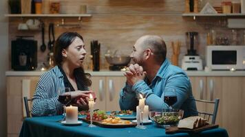 giovane caucasico uomo sorprendente donna con regalo durante festivo cena seduta a il tavolo nel il cucina. contento allegro coppia cenare insieme a casa, godendo il pasto festeggiare loro anniversario foto