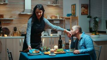 riflessivo moglie servendo entusiasta marito. Contentissimo donna preparazione festivo cena con sano cibo, cucinando per il suo uomo romantico cena, parlando, seduta a tavolo nel cucina, godendo il pasto foto