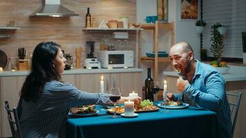 giovane Gli amanti mangiare sano cibo a cena. contento coppia parlando, seduta a tavolo nel cenare camera, godendo il pasto, festeggiare loro anniversario a casa avendo romantico volta. foto