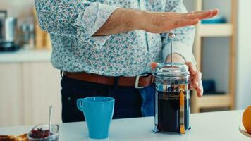 anziano uomo fabbricazione caffè utilizzando francese stampa durante prima colazione nel cucina. anziano persona nel il mattina godendo fresco Marrone bar caffè espresso tazza caffeina a partire dal Vintage ▾ tazza, filtro rilassare rinfresco foto