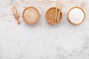 chicchi di grano, farina di grano marrone e farina di grano bianco in una ciotola di legno allestita su sfondo bianco di cemento. foto