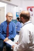 anziano uomo ricevere assistenza sanitaria trattamento a partire dal medico nel ospedale visita medica camera. anziano paziente avendo un' converstation con medico cose nel privato clinica durante consultazione. foto