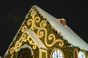 tetto con neve di un' Natale decorativo Casa, decorato con luminoso modelli e ghirlande. festivo nuovo anni inverno città illuminazione. foto