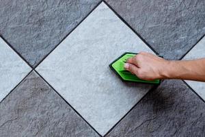 la vista dall'alto di una mano umana sta usando una lavapavimenti in plastica di colore verde per pulire il pavimento piastrellato con un detergente per pavimenti. foto