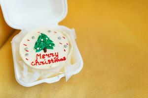 bianca Natale torta con un' verde albero e allegro Natale testo nel un' bianca scatola su un' giallo sfondo. foto