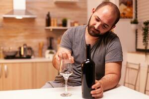 alcolizzato uomo essere depresso e frustrato Tenere bottiglia di rosso vino nel cucina. infelice persona malattia e ansia sensazione esausto con avendo alcolismo i problemi. foto