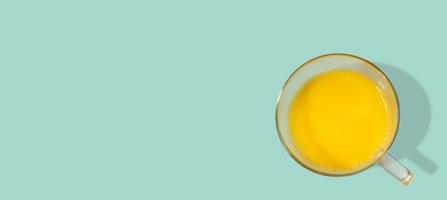 banner con un bicchiere pieno di succo d'arancia appena fatto con frutta fresca, a solido sfondo turchese con copia spazio. concetto di cibo sano, vitamine e vita sana. foto
