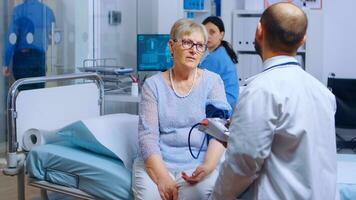 professionista le misure anziano pensionato donna sangue pressione con un' tenere sotto controllo mentre infermiera nel Lavorando nel il sfondo. assistenza sanitaria medico medicina sistema, trattamento e diagnosi di malattia visita medica foto