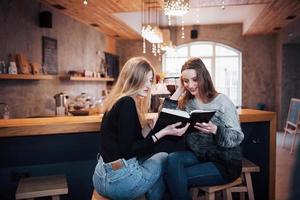 due ragazze assorte nella lettura di un libro durante la pausa al bar. carine e adorabili giovani donne stanno leggendo un libro e bevendo caffè foto
