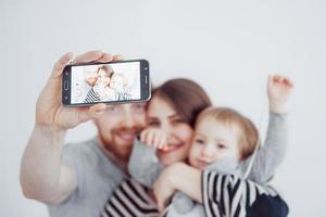 famiglia, vacanze, tecnologia e persone - madre, padre e bambina sorridenti che fanno selfie con la fotocamera su sfondo bianco foto