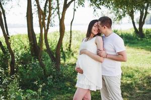 felice e giovane coppia incinta che si abbraccia nella natura foto