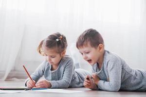 i bambini si sdraiano sul pavimento in pigiama e disegnano con le matite. bambino carino dipinto con le matite foto