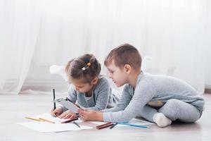 i bambini si sdraiano sul pavimento in pigiama e disegnano con le matite. bambino carino dipinto con le matite foto