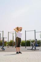 donna felice che si allena sul campo sportivo nella soleggiata giornata estiva, alzando le braccia, godendosi il sole foto