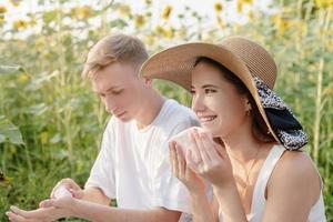 giovane coppia che fa picnic sul campo di girasoli al tramonto, asciugandosi le mani e il viso foto