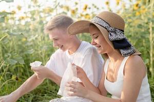 giovane coppia che fa picnic sul campo di girasoli al tramonto, asciugandosi le mani e il viso foto