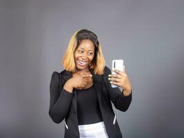 nero africano donna utilizzando inteligente Telefono In piedi al di sopra di un' studio parete foto