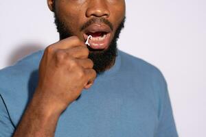 giovane nero uomo utilizzando un' filo per pulito il suo denti vicino su foto