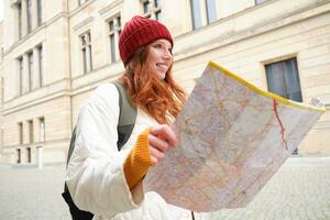 testa Rossa ragazza, turista esplora città, sembra a carta carta geografica per trova modo per storico punti di riferimento, donna su sua viaggio in giro Europa ricerche per giro turistico foto