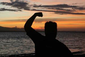 silhouette di un' giovane uomo in piedi di il lago godendo il tramonto. tranquillo, calmo atmosfera nel natura foto