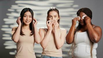 giovane Modelli fare tre saggio scimmie cartello con cotone pastiglie, la creazione di bellezza cura della pelle campagna nel studio. diverso donne avendo divertimento giocando in giro con cosmetici, detergente pelle. foto