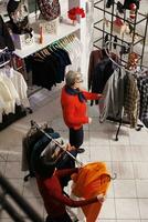 multiplo clienti guardare per natale i regali e festivo abbigliamento, persone fabbricazione preparazioni per Natale vigilia feste e tradizione. Al dettaglio memorizzare i clienti shopping per Abiti durante dicembre stagione. foto