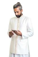 ai generato elegante indiano uomo vestito nel un' bianca completo da uomo e indossare un' turbante, guardare a il suo smartphone. foto