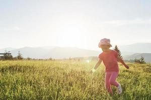 carino felice piccola bambina gioca all'aperto nel prato e ammirando la vista sulle montagne. copia spazio per il tuo testo foto