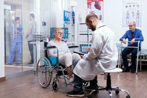 non valido anziano donna seduta nel sedia a rotelle nel ospedale camera con medico scrittura recupero trattamento. uomo con disabilità ,a passeggio telaio seduta nel ospedale letto. Salute cura sistema, clinica pazienti. foto