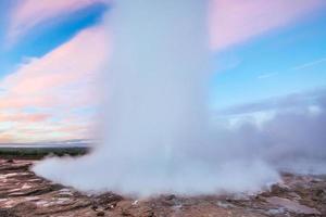 eruzione del geyser strokkur in islanda. colori fantastici brillano attraverso il vapore. bellissime nuvole rosa in un cielo azzurro foto