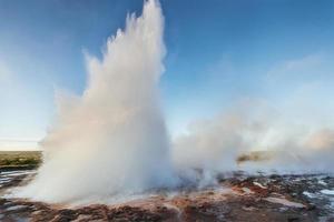 eruzione del geyser strokkur in islanda. colori fantastici brillano attraverso il vapore. bellissime nuvole rosa in un cielo azzurro foto