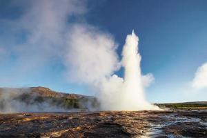 eruzione del geyser strokkur in islanda. colori fantastici brillano attraverso il vapore. bellissime nuvole rosa in un cielo azzurro foto