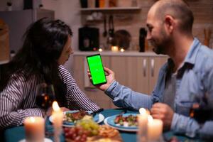 coppia guardare a Telefono con verde finto su avendo romantico cena. contento Tenere Telefono verde schermo modello croma chiave isolato smartphone Schermo utilizzando tecnologia Internet. foto