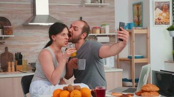 contento giovane coppia assunzione selfie durante prima colazione. gioioso sposato marito e moglie fabbricazione divertente facce mentre assunzione un' foto durante prima colazione nel cucina.