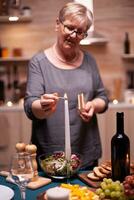 candela ardente su tavolo per romantico cena di anziano coppia nel cucina. anziano donna in attesa sua marito per un' romantico cena. maturo moglie preparazione festivo pasto per anniversario celebrazione. foto