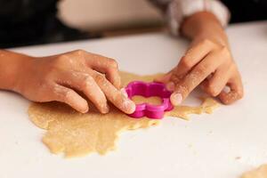 avvicinamento di nipote mani fabbricazione tradizionale biscotto dolce utilizzando natale Impasto forma festeggiare Natale vacanza nel x-mas decorato cucina. bambino godendo inverno stagione cucinando fatti in casa Pan di zenzero foto