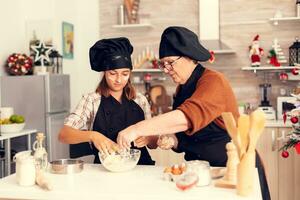 ragazzo fabbricazione tradizionale biscotti su Natale giorno indossare grembiule e ossatura. contento allegro gioioso adolescenziale ragazza porzione anziano donna preparazione dolce biscotti per celebrare inverno vacanze. foto